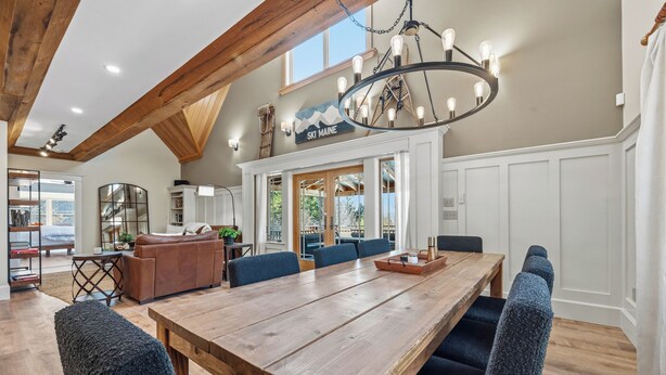 A spacious dining area with a long wooden table, blue upholstered chairs, and a chandelier. - Moose Ridge Haven | Spacious and beautifully appointed home | Hot tub & Sauna (Rangeley)