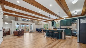 A spacious kitchen with wooden beams, a bar area, and a dining space with chairs and a sofa. - Moose Ridge Haven | Spacious and beautifully appointed home | Hot tub & Sauna (Rangeley)