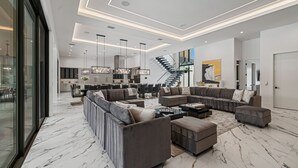 Un salon moderne avec un canapé d’angle, un pouf et un mur en verre.