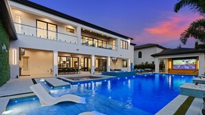 Une maison moderne à deux étages, dotée d’une grande piscine, d’un espace extérieur aménagé et d’un balcon bien éclairé.