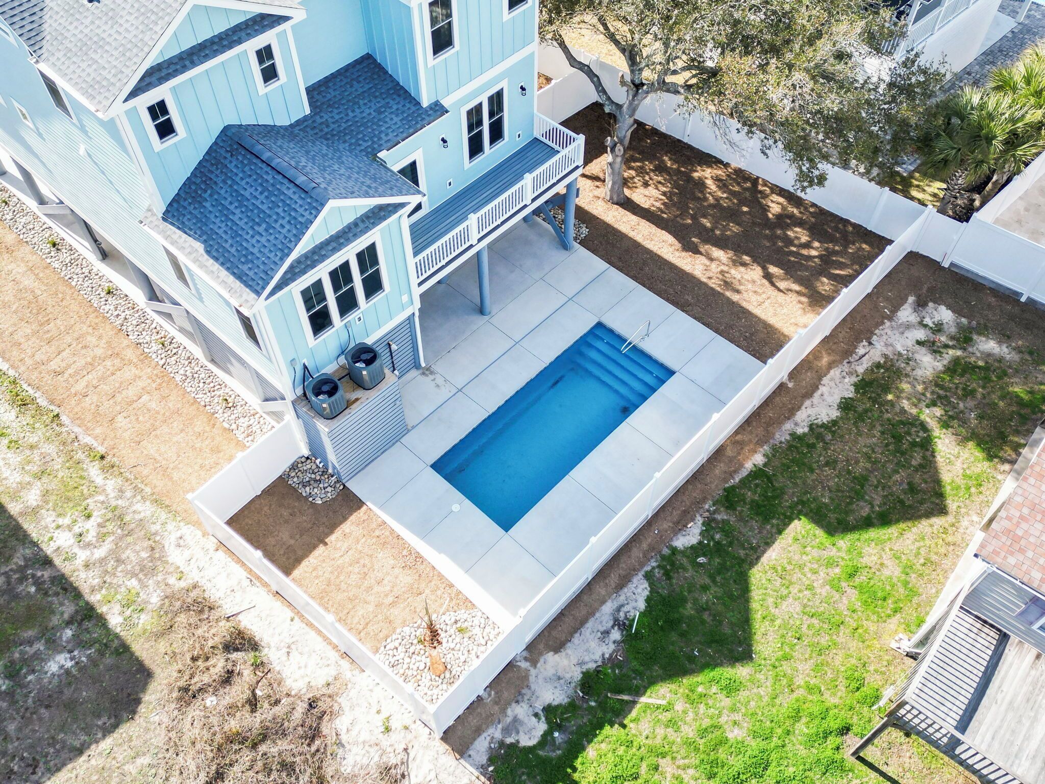 Una casa de dos pisos con piscina, patio cubierto y jardín cercado.
