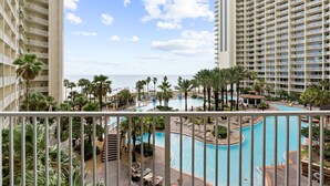 A hotel pool area with multiple swimming pools, palm trees, and a view of the ocean.