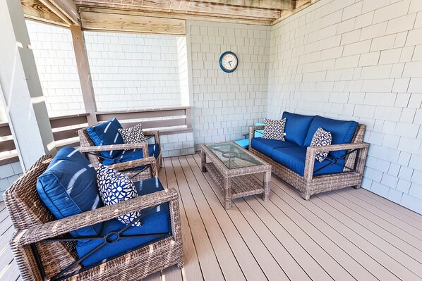 A covered outdoor seating area with wicker furniture and a glass coffee table.