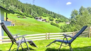 A terrace with two lounge chairs overlooking a green hillside with houses and a power line tower. - Nice apartment for 3 people with WIFI, TV and terrace (Wenns)