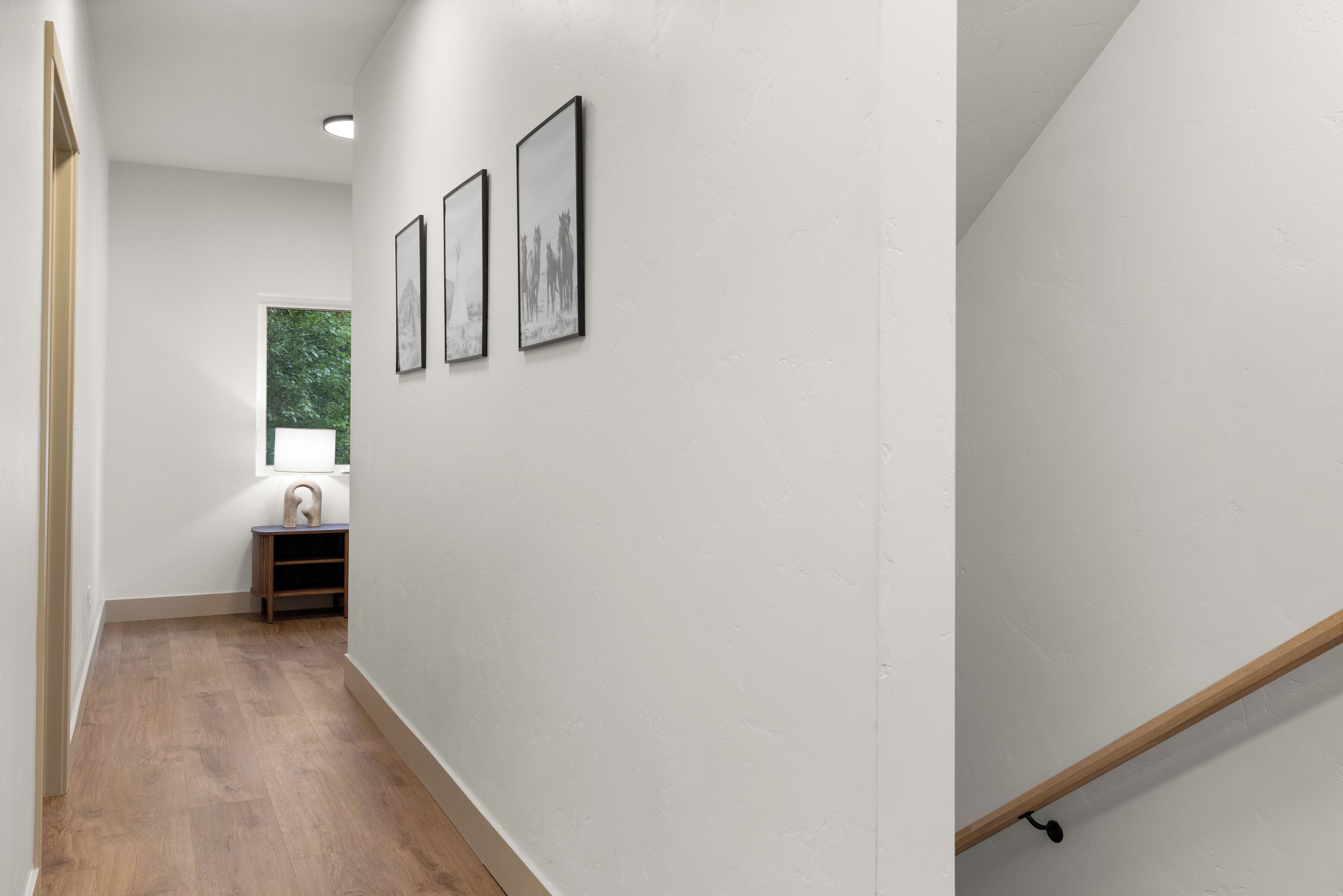 A hallway with wooden flooring, white walls, and three framed pictures.