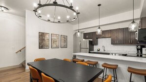 A modern kitchen with dark wooden cabinets, a white countertop, and a black dining table with orange chairs.