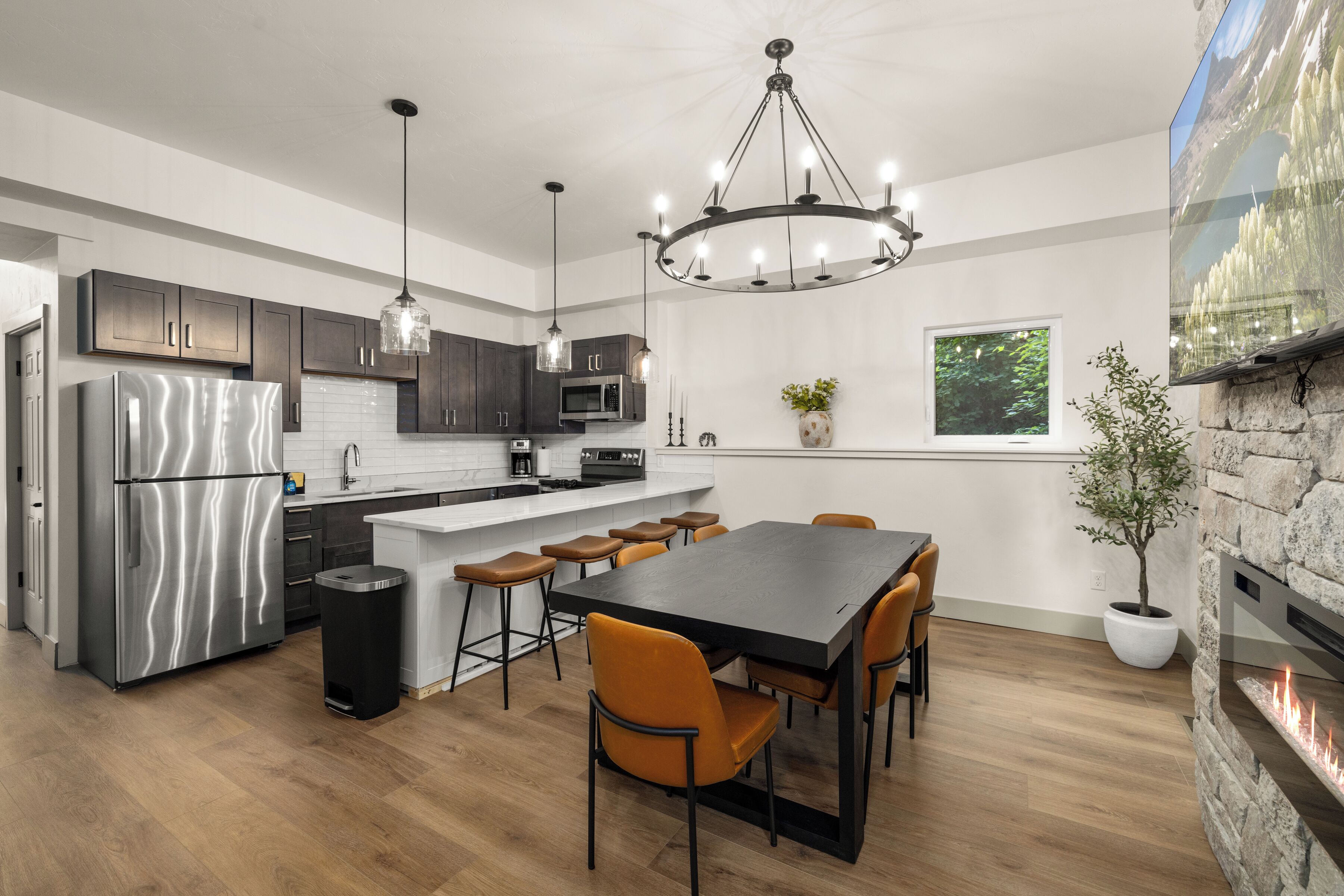 Une cuisine moderne dotée d’un îlot central, d’appareils électroménagers en acier inoxydable, de luminaires suspendus et d’une cheminée en pierre.