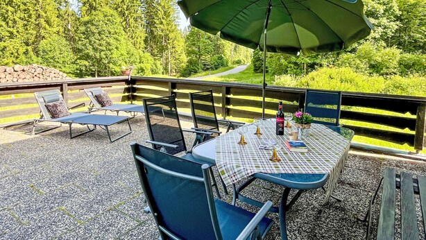 Une terrasse extérieure avec une table et des chaises, un parasol vert et une vue sur une zone boisée.