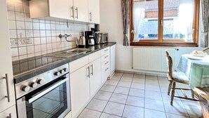 Une cuisine avec des meubles blancs, un plan de travail noir, une cuisinière et une fenêtre avec des rideaux.