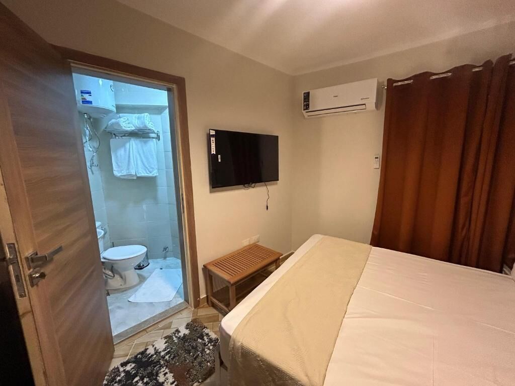 A bedroom with a bed, a television, an air conditioning unit, and a shower area.
