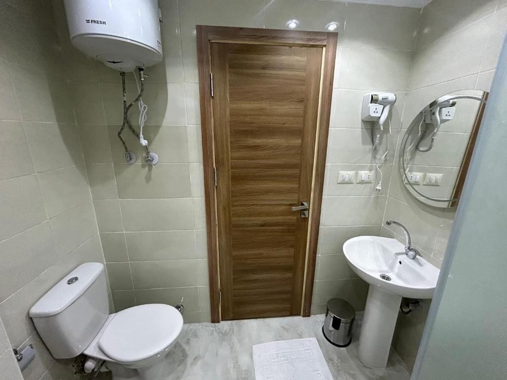A bathroom with a wooden door, white toilet, and a sink with a mirror.