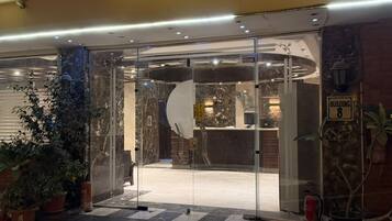 Entrada de hotel con puerta de vidrio, mostrador de recepción y un cartel con el número del edificio.