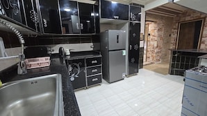 Cocina con gabinetes negros, refrigerador de acero inoxidable y piso de baldosas.