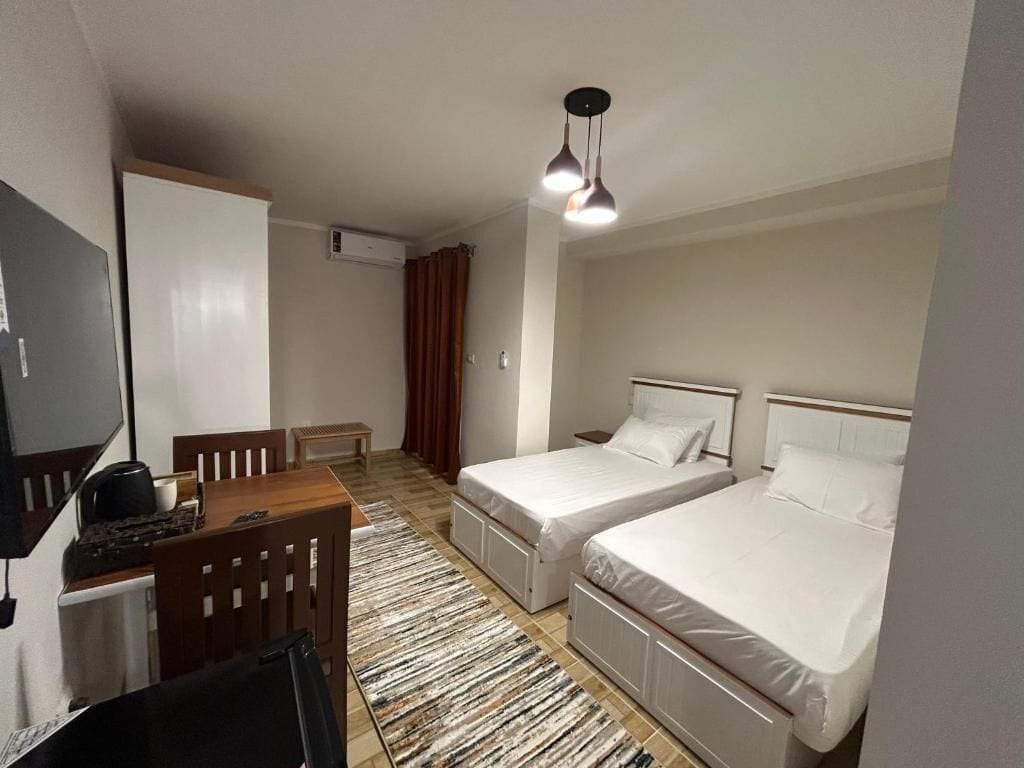 Een hotelkamer met twee bedden, een bureau met stoel, een televisie en een plafondlamp.