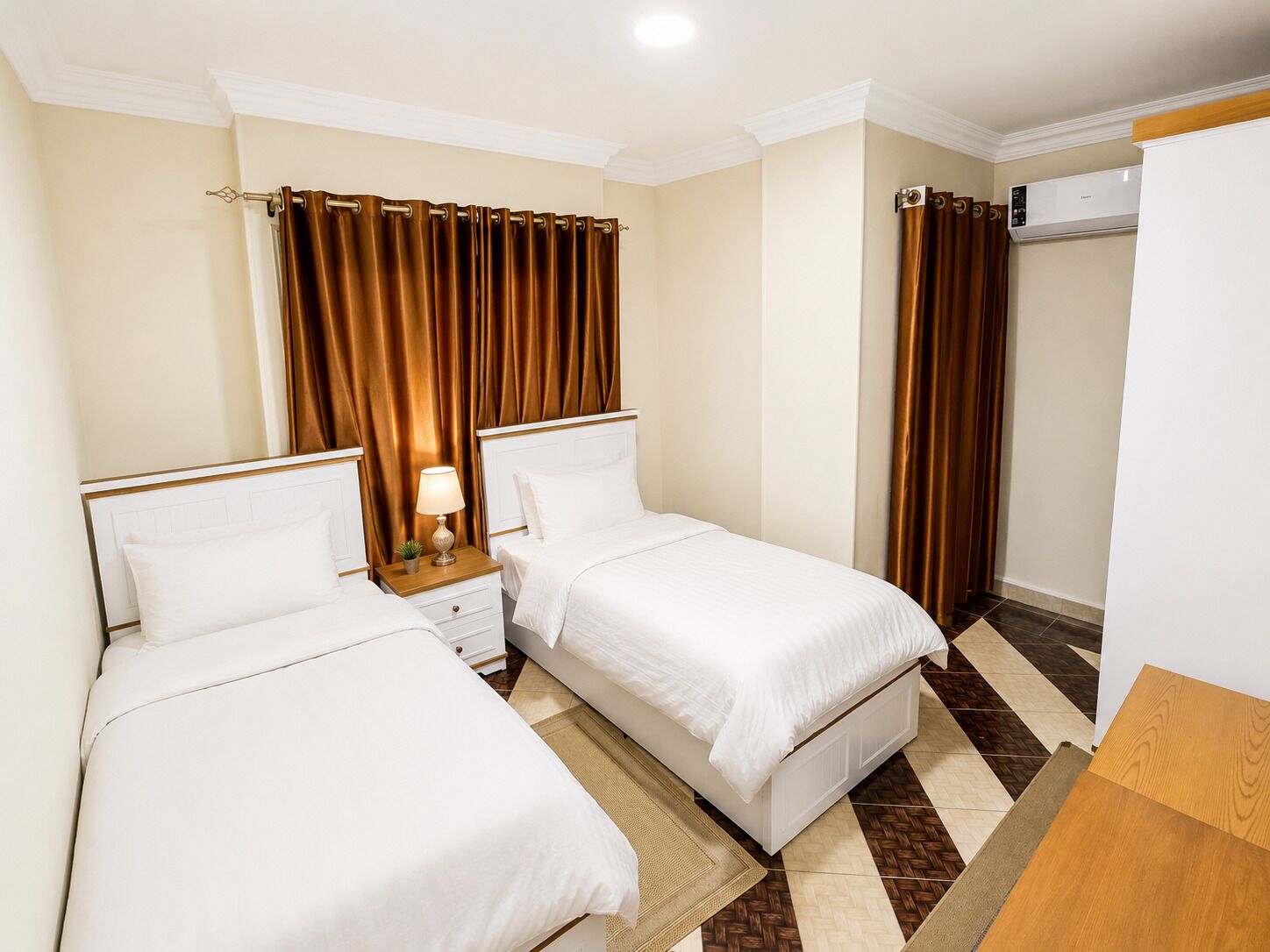 Ein Hotelzimmer mit zwei Einzelbetten, einem Nachttisch mit Lampe, einem großen Spiegel und einem Kleiderschrank.
