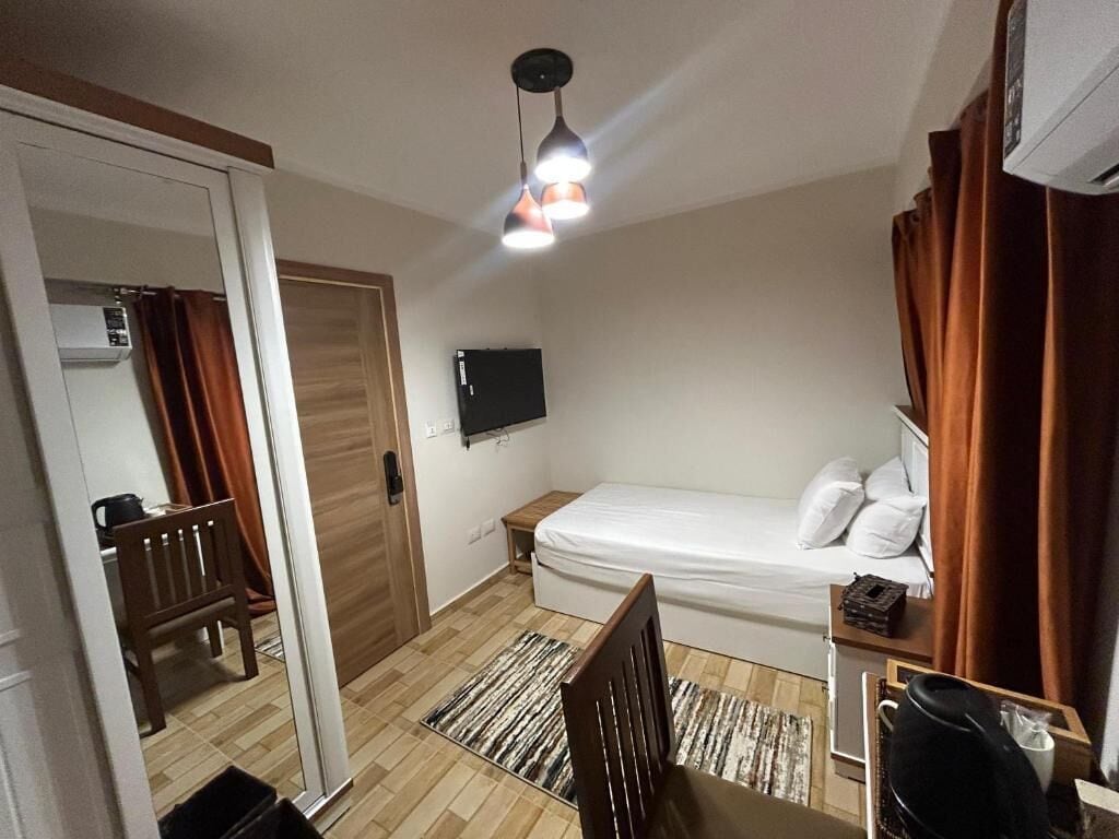 A compact hotel room with a single bed, a small desk, a chair, a television mounted on the wall, and a ceiling light fixture.