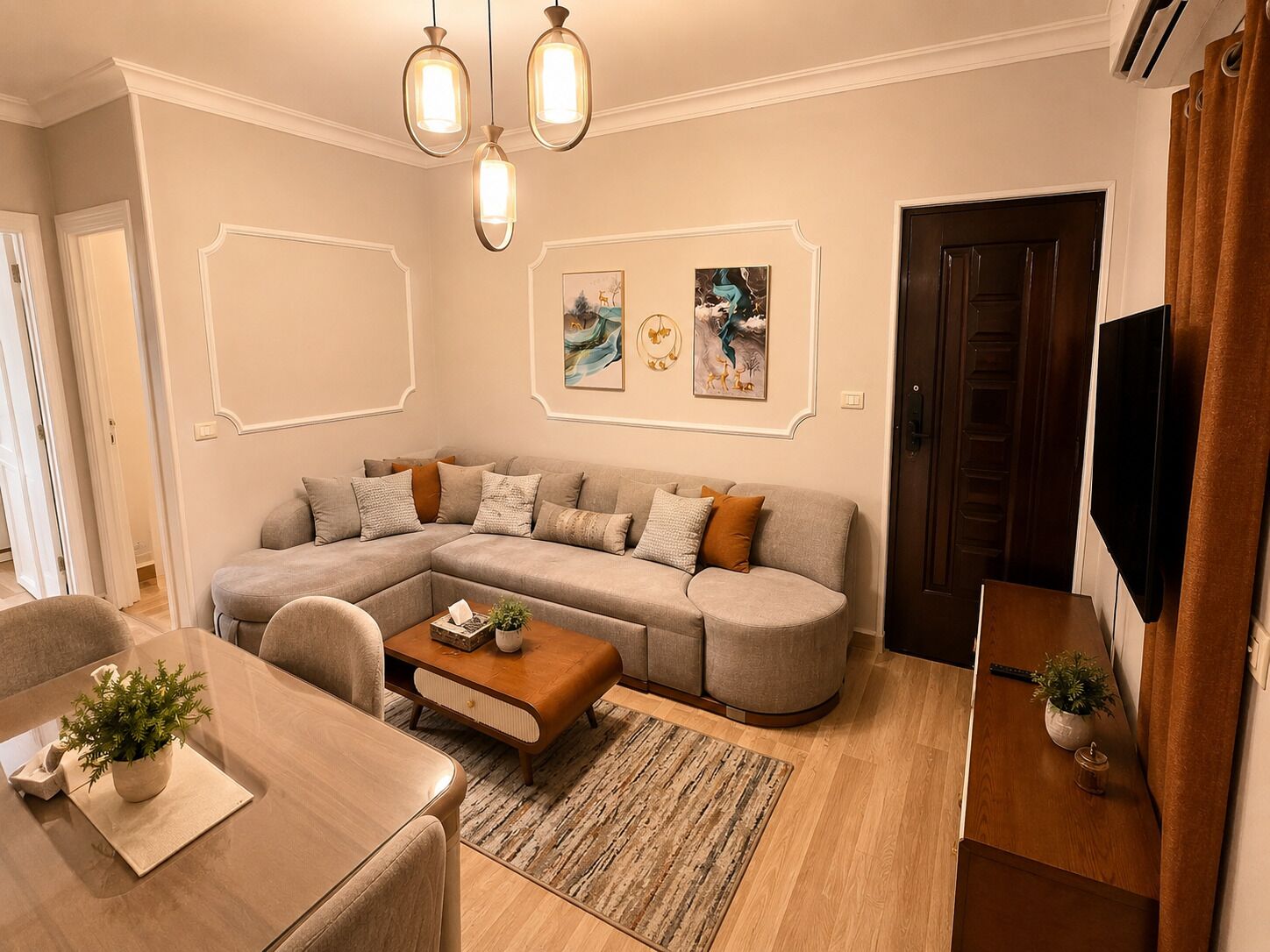 Una sala de estar con un sofá modular, una mesa de centro y un televisor. Hay luces empotradas en la pared y obras de arte.
