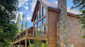 A log cabin with a stone chimney, large windows, and a deck extending over a rocky ground. - Log Cabin w/ Billiards & Table Tennis - Mtn Views, 24mi Breck, Pet-Friendly (Fairplay)