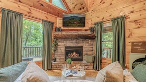 A cozy cabin interior with a stone fireplace, wooden walls, and a television mounted above it.