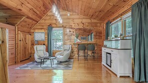 A cozy cabin interior with wooden walls, a dining area, and a seating space with chairs and a table.