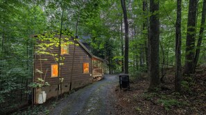 A wooden cabin with a porch, surrounded by a forested area. - Romantic Escape for 2• Views, HotTub, Sauna & Dogs (Sevierville)
