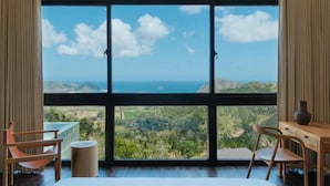 A bedroom with a large window offering a view of a coastal landscape. - DUNIA LOMBOK (Selong Belanak)