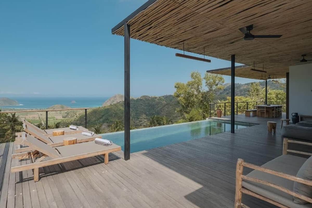 Une terrasse en bois avec une piscine, des chaises longues et une table offrant une vue panoramique.