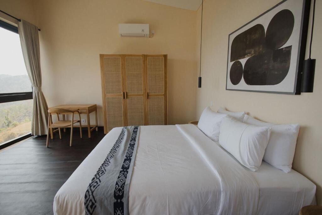 Ein Schlafzimmer mit einem großen Bett, einem Holzschrank, einem Schreibtisch und Blick durch ein Fenster.
