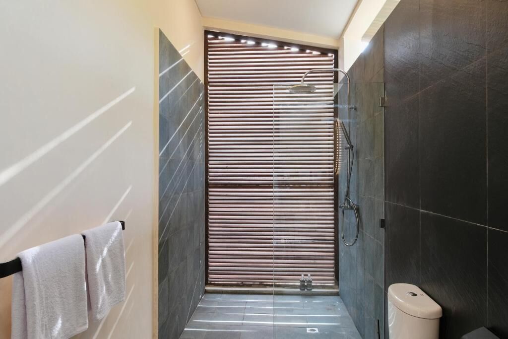 A narrow shower area with a sliding door, dark tiled walls, and a white toilet.