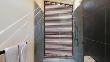 A narrow shower area with a sliding door, dark tiled walls, and a white toilet.