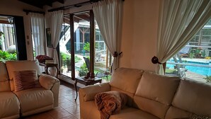 Ein großzügiger Wohnbereich mit einem beigen Sofa, einem Couchtisch und Blick auf einen Swimmingpool und Außenbereich.