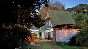 Ein Weg führt zu einem Haus mit grüner Dachbegrünung, umgeben von üppigem Grün und einer Vögelspapagei-Blüte.