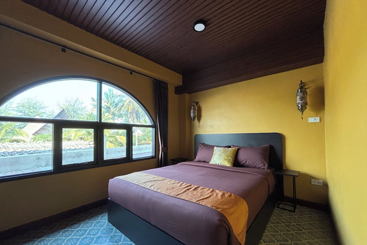 Une chambre à coucher avec un lit, une fenêtre, une lampe fixée au mur et un sol à motifs.
