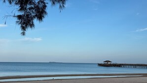 A beach with a pier extending into calm waters, clear skies, and sparse vegetation. - Phoenix Room (Pathio)