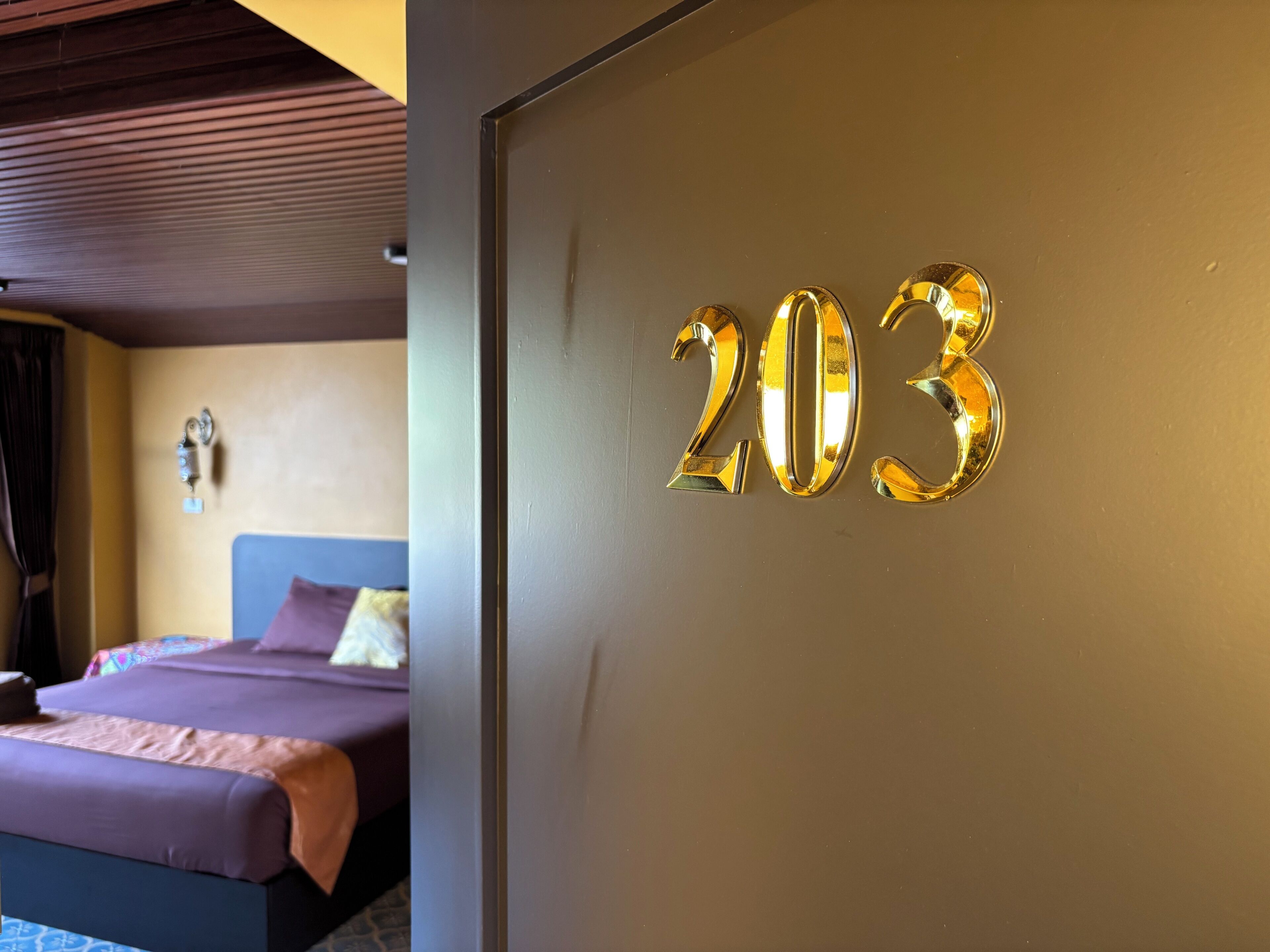 Una habitación con una cama, una pared con el número 203 y un techo con detalles de paneles de madera.