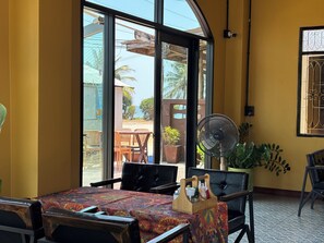 A room with a large window, a fan, a table with a patterned tablecloth, and a wooden tray with items. - Phoenix Room (Pathio)