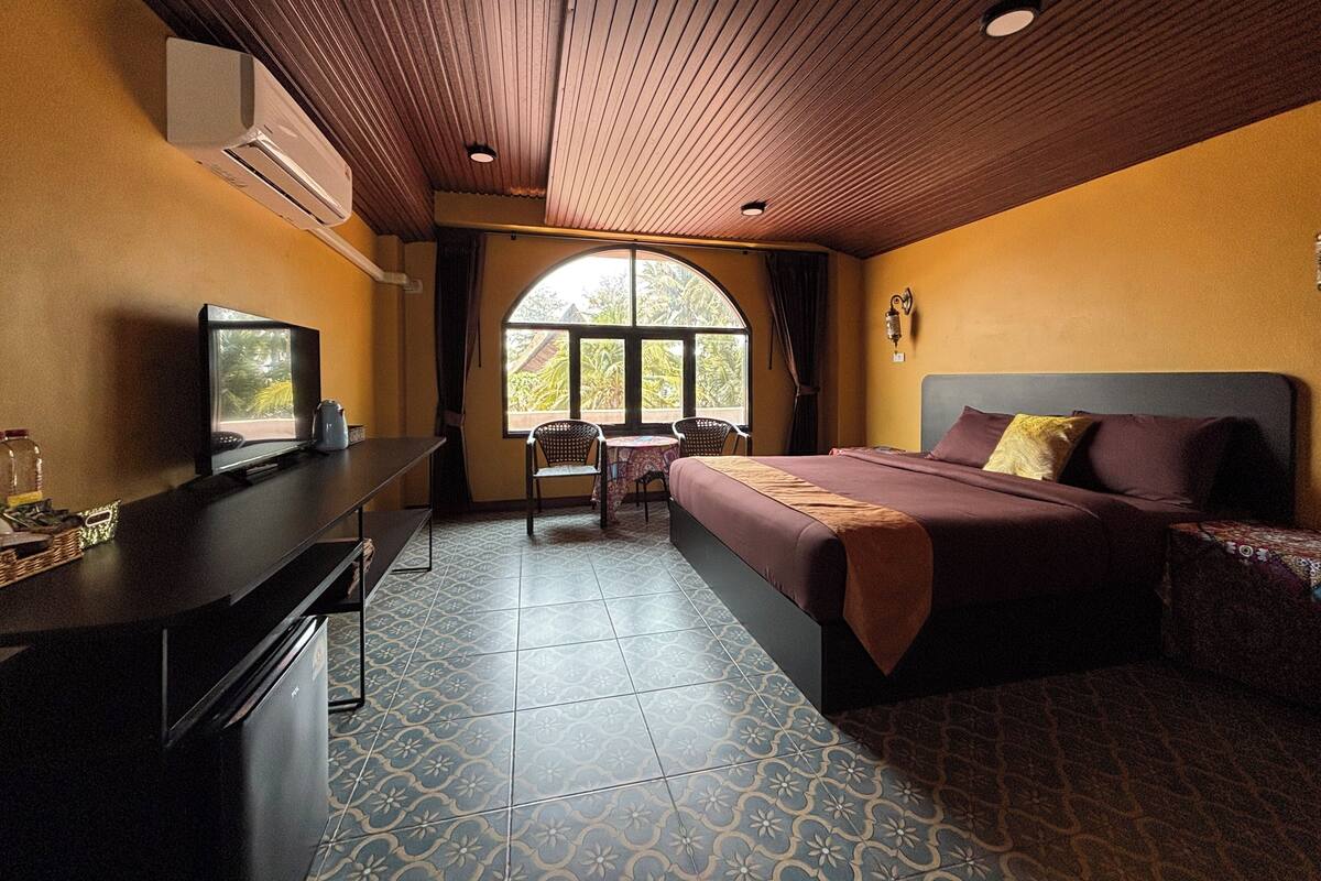 Une chambre d’hôtel avec un lit, un bureau avec une télévision, une chaise et une fenêtre donnant sur un paysage verdoyant.