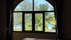A room with a bed, a window with a view of palm trees and a beach. - Phoenix Room (Pathio)