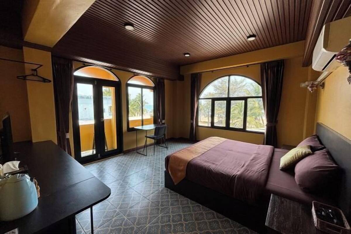 Une chambre d’hôtel avec un lit, un bureau et une chaise. Il y a des fenêtres avec des rideaux, et un appareil de climatisation est fixé au mur.