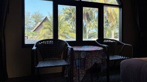 A room with a large arched window, two wicker chairs, a small table, and a bed. - Phoenix Room (Pathio)