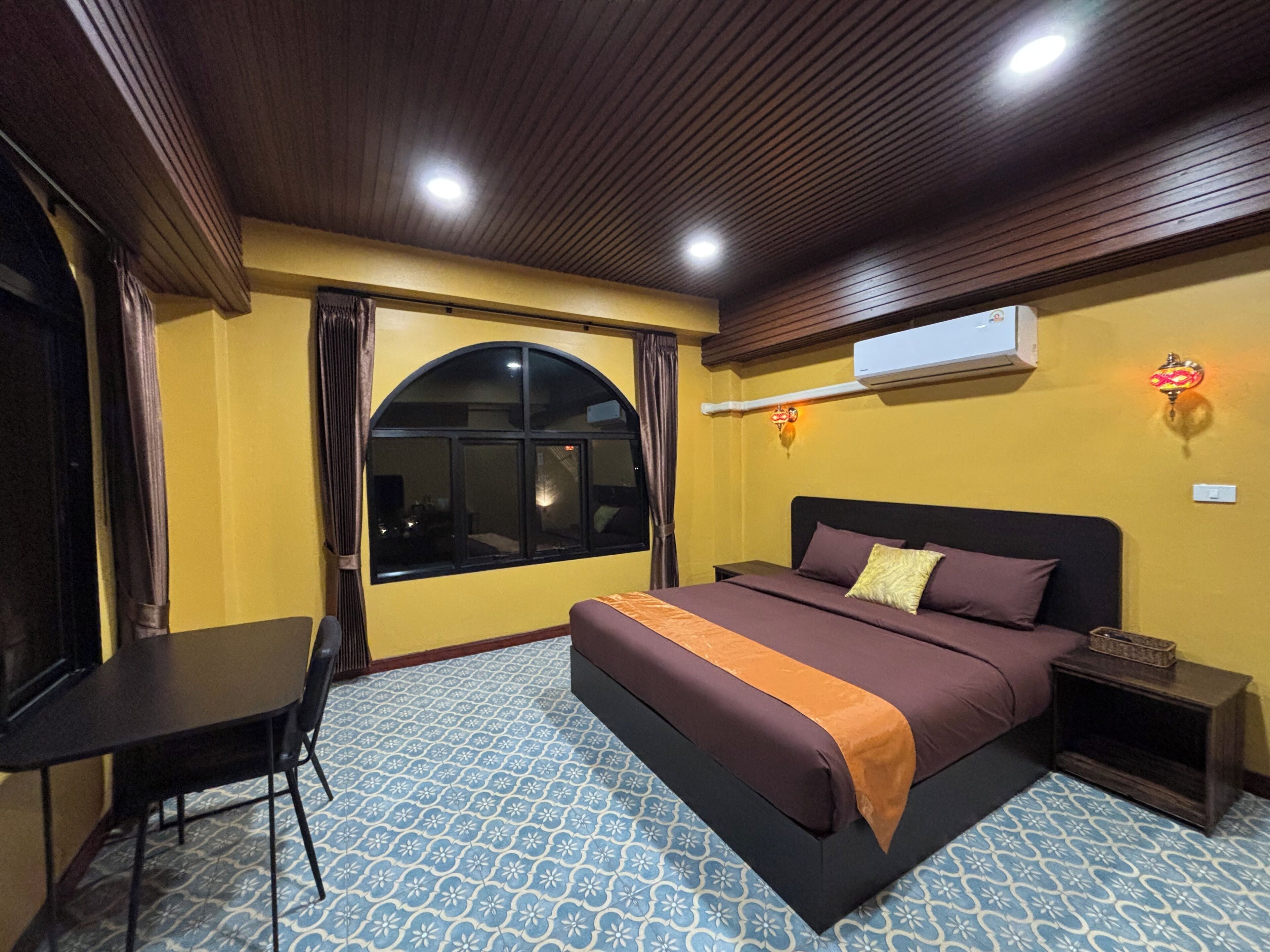 Una habitación de hotel con cama, escritorio, silla, ventana y aire acondicionado.