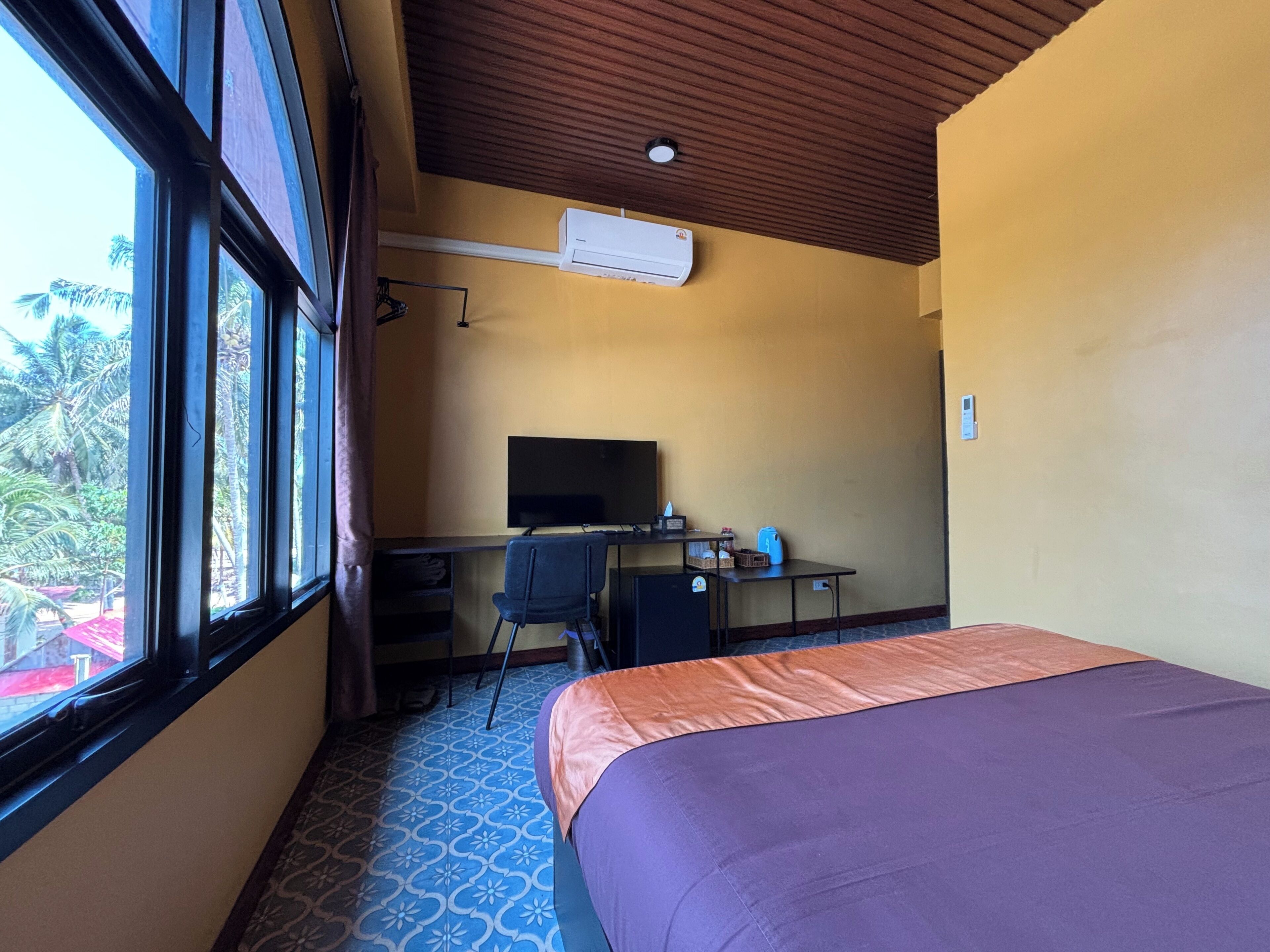Una habitación con cama, un escritorio con computadora, televisor y aire acondicionado.