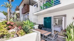A two-story building with a balcony, a patio with a table and chairs, and a bedroom with a bed and a window. - Spacious 8BR Tri-Level Home w/ Ocean Views, Multiple Patios, Steps to 43rd St Beach (Newport Beach)