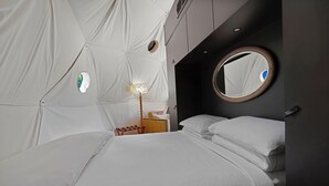Un dormitorio moderno con una cama, una mesita de noche, una lámpara, un espejo redondo y una ventana circular empotrada en la pared.