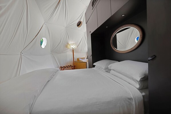 Une chambre moderne comprenant un lit, une table de chevet, une lampe, un miroir rond et une fenêtre circulaire fixée au mur.