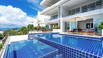 Un hotel moderno con una amplia piscina exterior, varios balcones y vistas a la montaña.