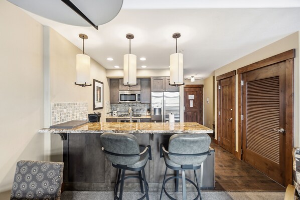 A kitchen with a central island, bar stools, pendant lighting, and wooden doors.