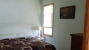 A bedroom with a bed, a nightstand, a dresser, a window with blinds, and a painting on the wall. - Rustic 2 Bed Lakeside Cabin - boats available (Hayward)