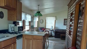 A compact kitchen with wooden cabinets, a gas stove, and a dining area with a table and chairs. - Rustic 2 Bed Lakeside Cabin - boats available (Hayward)