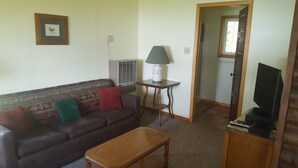 A living room with a sofa, a coffee table, a lamp, and a television. - Rustic 2 Bed Lakeside Cabin - boats available (Hayward)